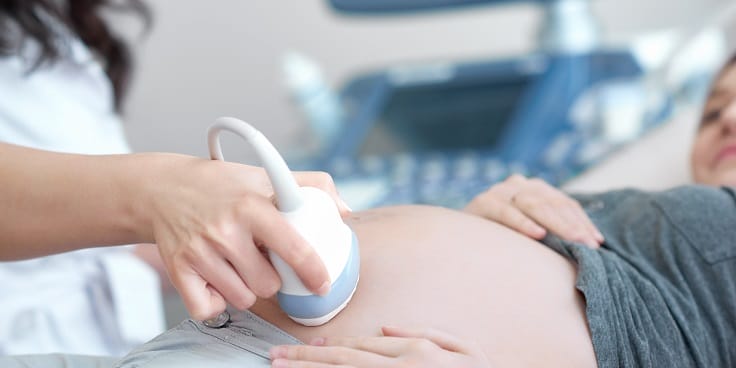 Arzt verwendet Ultraschallgerät zur Untersuchung einer schwangeren Frau.