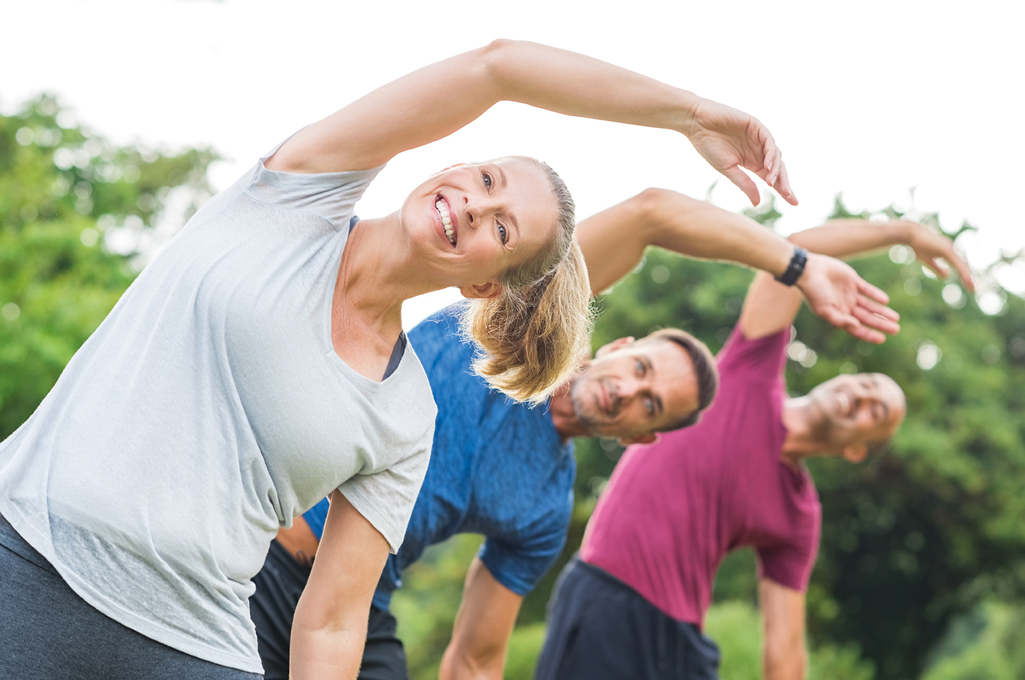 Eine junge Personengruppe führt Stretching Übungen im Park aus.