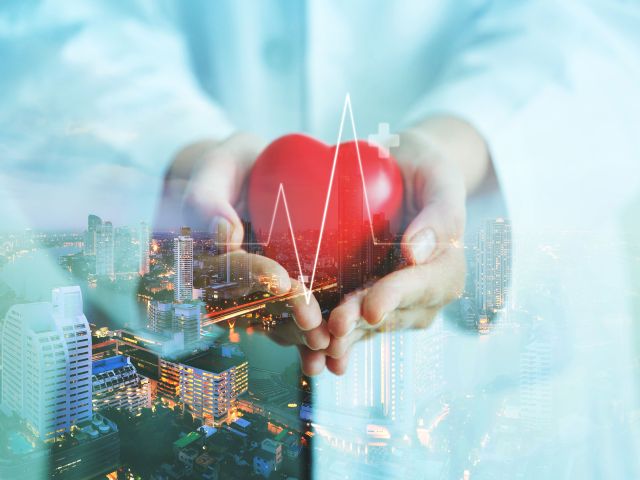 Herz in Händen vor einer Stadtlandschaft mit EKG-Linie, symbolisiert Gesundheit und Urbanisierung