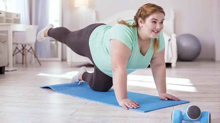 Frau mit Adipositas turnt auf einer Gymnastikmatte